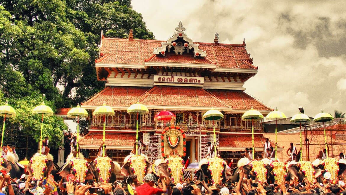 A grand Kerala temple during a vibrant religious festival, with caparisoned elephants, ceremonial umbrellas, and large crowds gathered for worship. The scene reflects the temple traditions, Hindu religious practices, and cultural heritage closely associated with the Nair community and Kerala society.